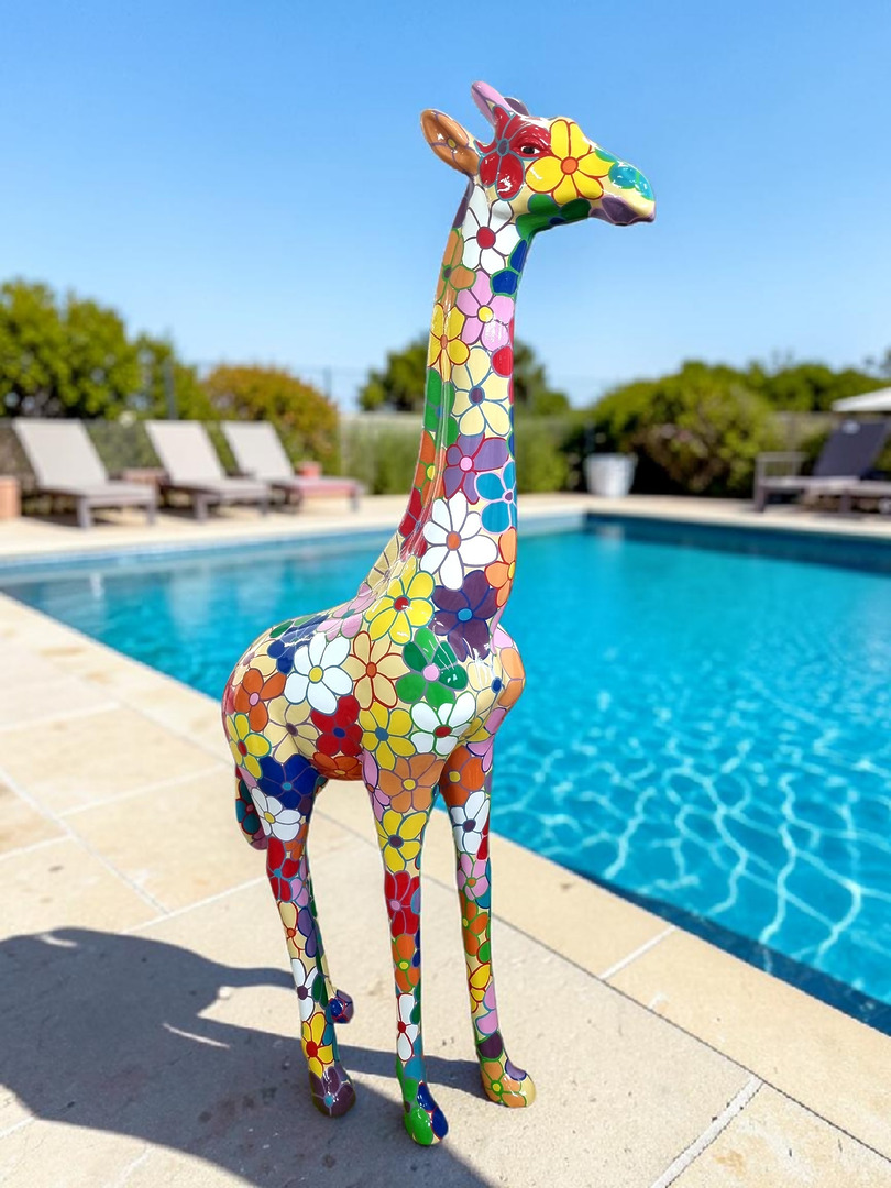 Handbemalte Giraffenskulptur mit bunten Blumenmustern neben einem Swimmingpool.